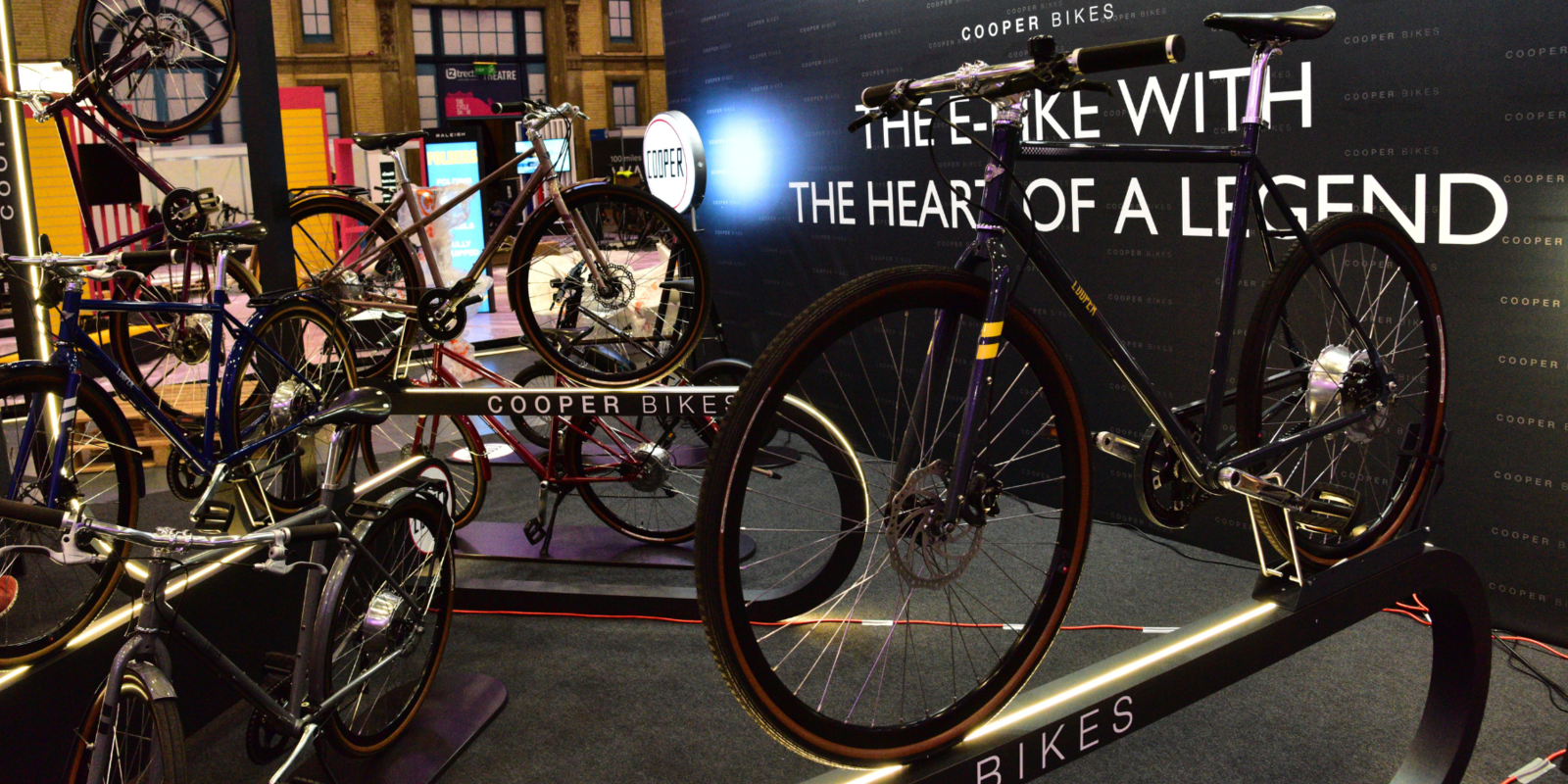 Cooper Bikes Messefläche mit beleuchteten Präsentern und großer schwarzer Rückwand mit Logo in London von Schemberg Ladenbau gestaltet