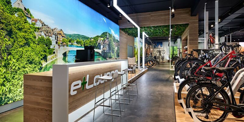 Neuer Verkaufsraum von eBiker in Laufenburg mit beleuchteten großformatigen Imagebildern und einer Cafe-Lounge nach der Umgestaltung durch Schemberg Ladenbau