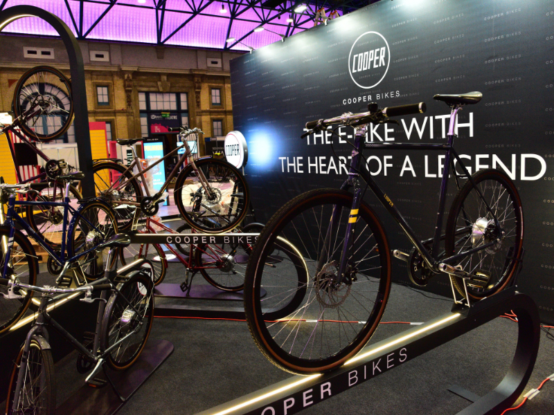 Cooper Bikes Messefläche mit beleuchteten Präsentern und großer schwarzer Rückwand mit Logo in London von Schemberg Ladenbau gestaltet