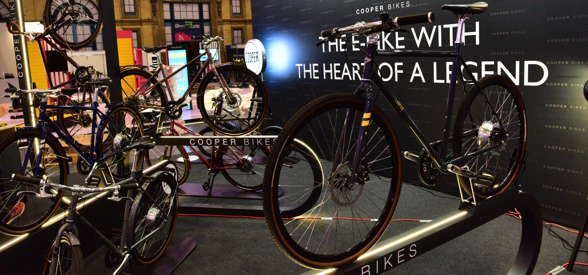 Cooper Bikes Messefläche mit beleuchteten Präsentern und großer schwarzer Rückwand mit Logo in London von Schemberg Ladenbau gestaltet