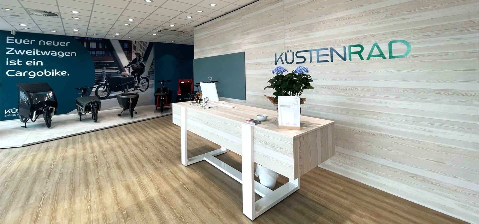 Neuer Verkaufsraum von Küstenrad in Kaltenkirchen mit großformatigen Imagebildern und Podesten für Fahrräder und Verkaufstresen nach der Umgestaltung durch Schemberg Ladenbau