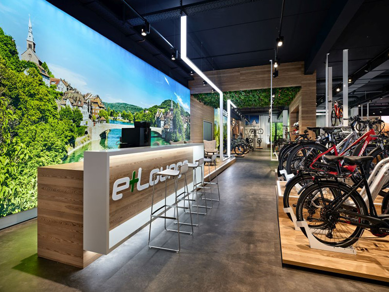 Neuer Verkaufsraum von eBiker in Laufenburg mit beleuchteten großformatigen Imagebildern und einer Cafe-Lounge nach der Umgestaltung durch Schemberg Ladenbau